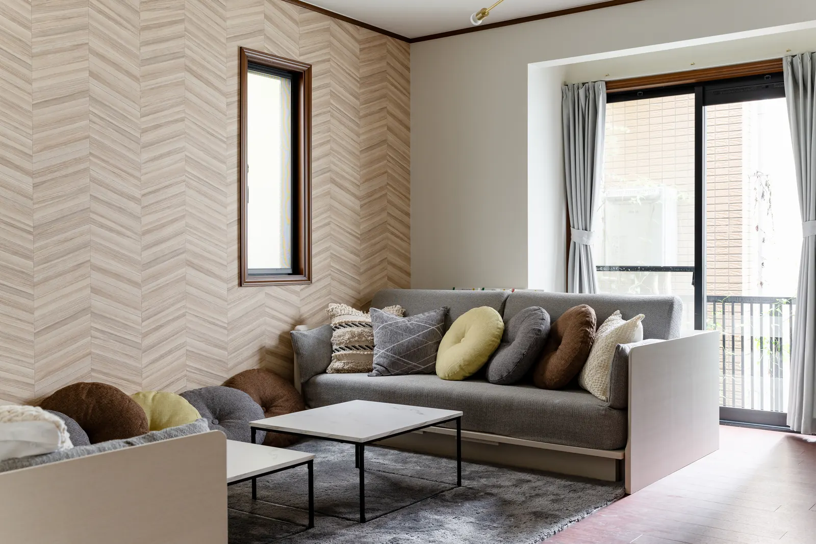 Living room of Hotel MADO Kitasando with two grey sofas that convert to double beds, cushions and a low marble table, opening onto a balcony